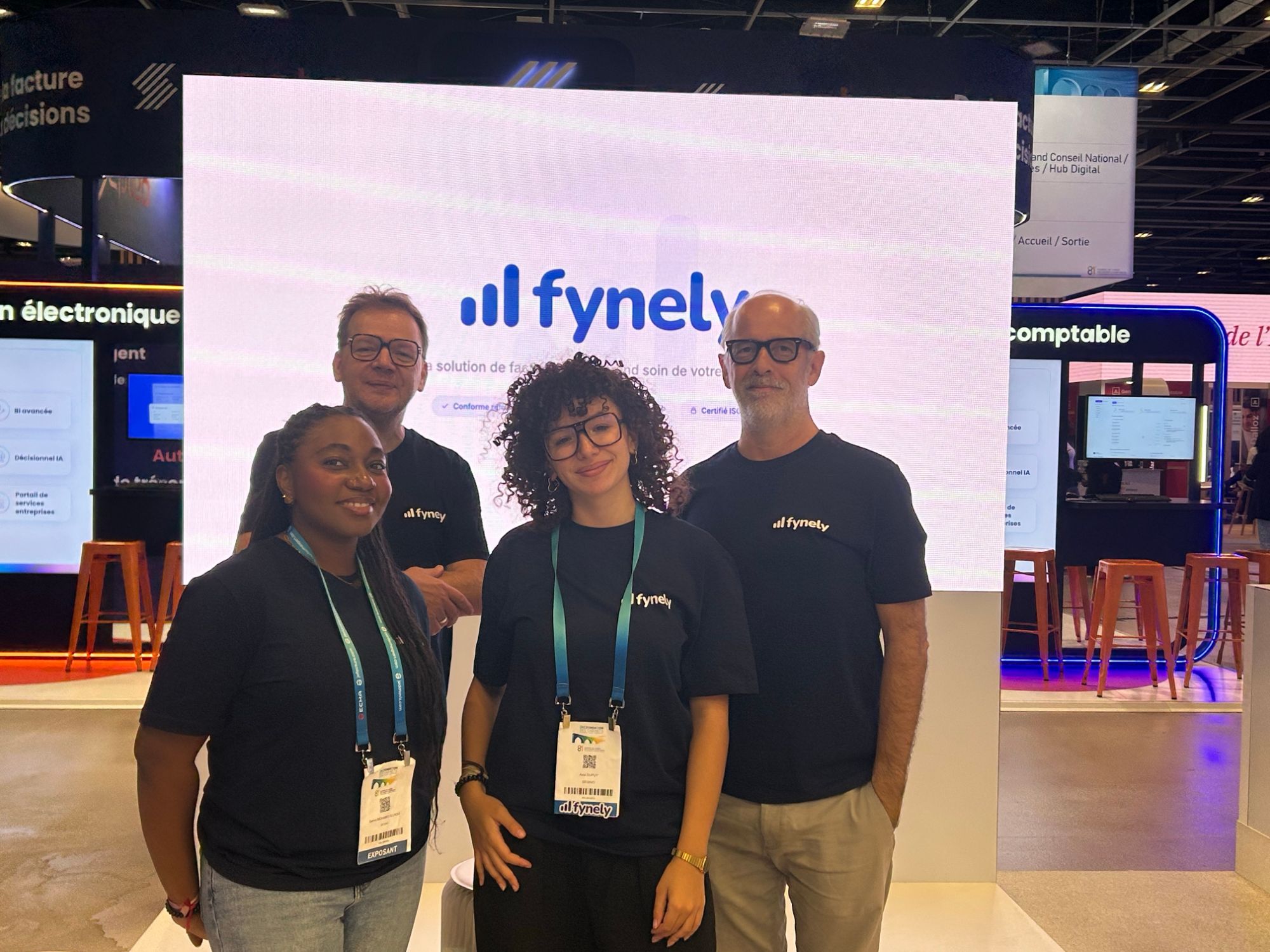 L'équipe Fynely sur le stand, devant l'écran d'accueil aux couleurs de la marque, au 81e congrès de l'Ordre des experts-comptables